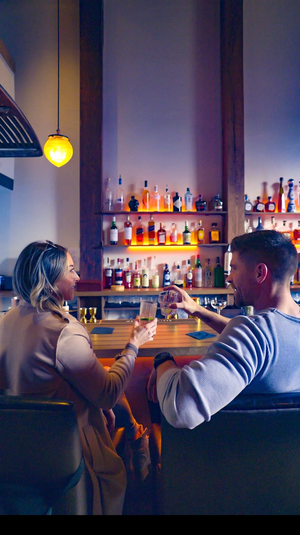 Guests toasting at the bar with the backlit shelves behind them.
